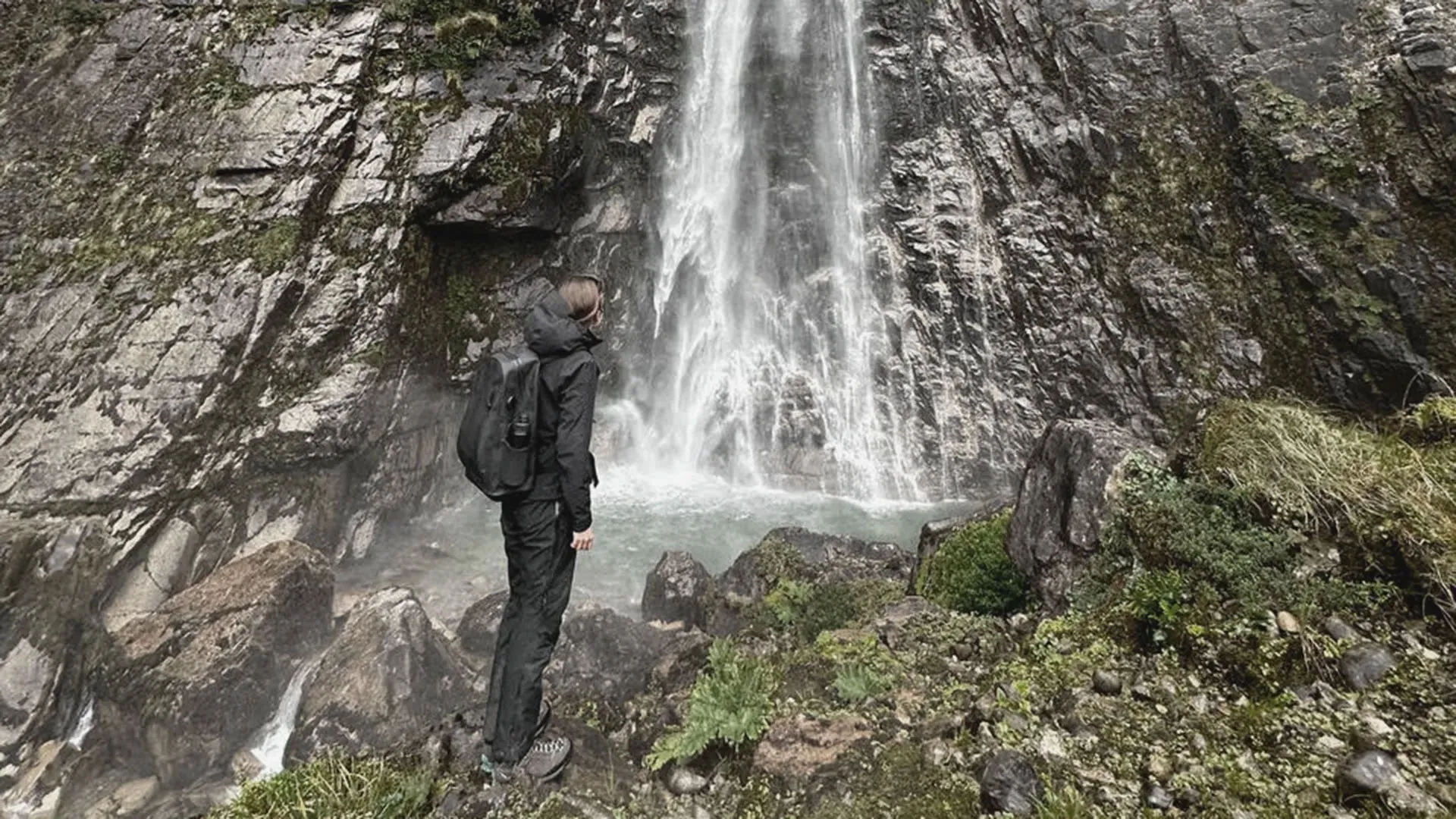 Hiker at the base of a tall Patagonian waterfall, backpack on